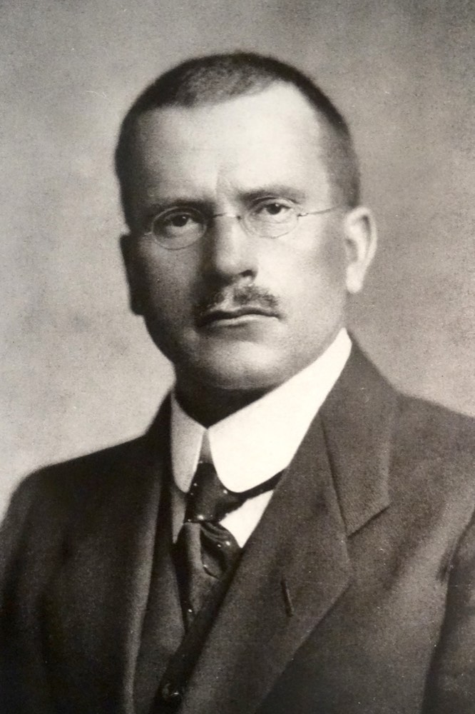 Black-and-white photographic portrait of an older Carl Jung in a suit and tie.
