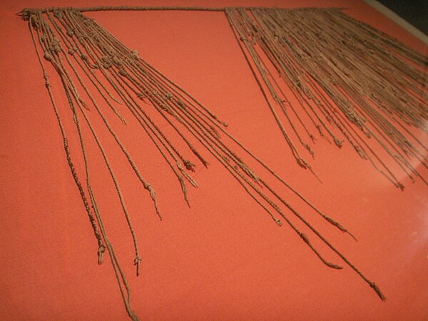 An Inca quipu specimen with colored knotted cords hanging from a primary cord, displayed at the Museo de la Nación in Lima.