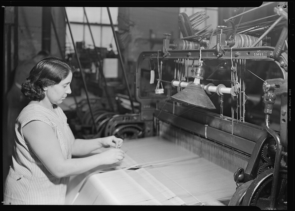 A weaver working with warp threads on the back side of a textile loom in Paterson, New Jersey.