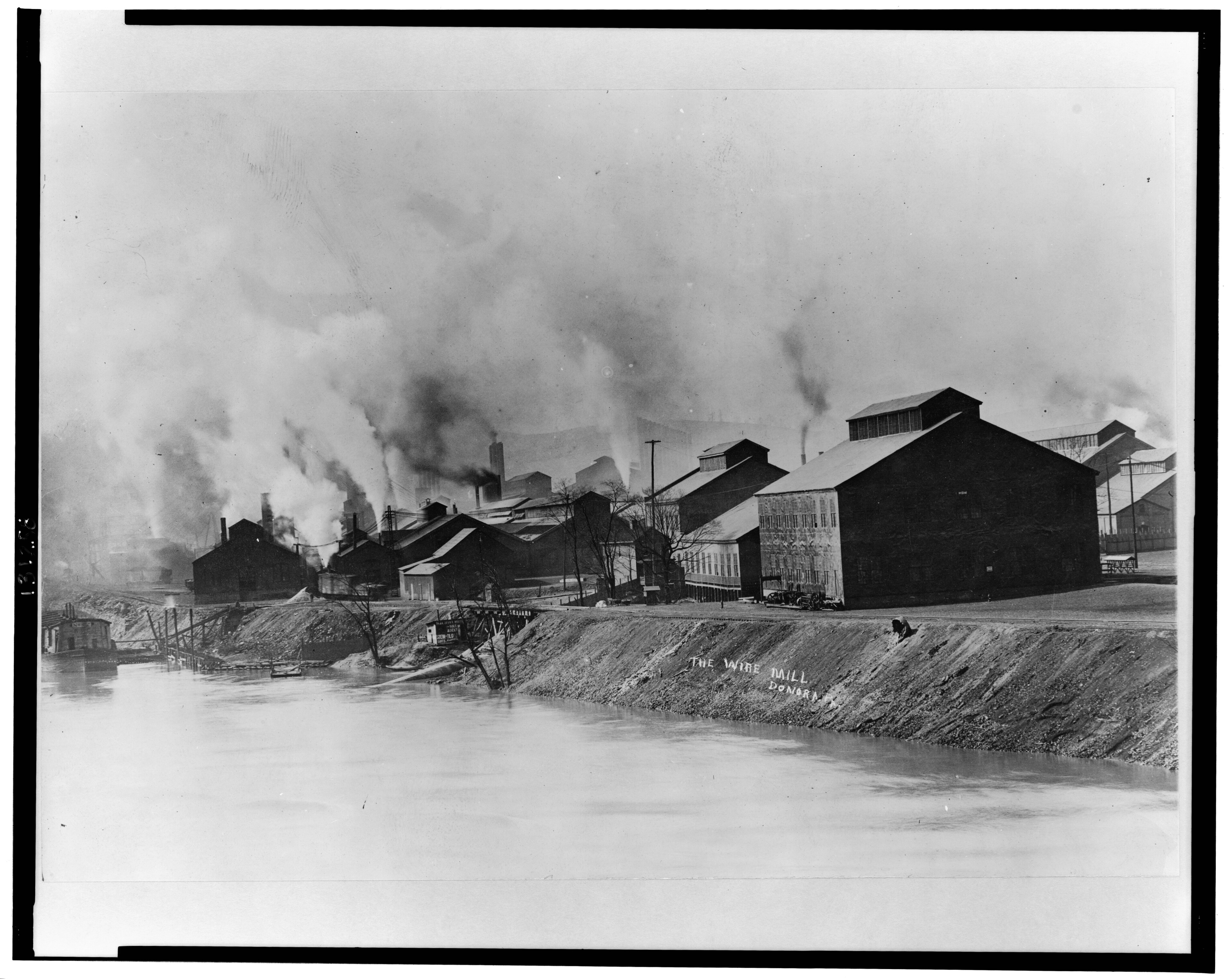 A large wire mill in Donora, Pennsylvania, with smokestacks and mill structures rising directly above a residential neighborhood.