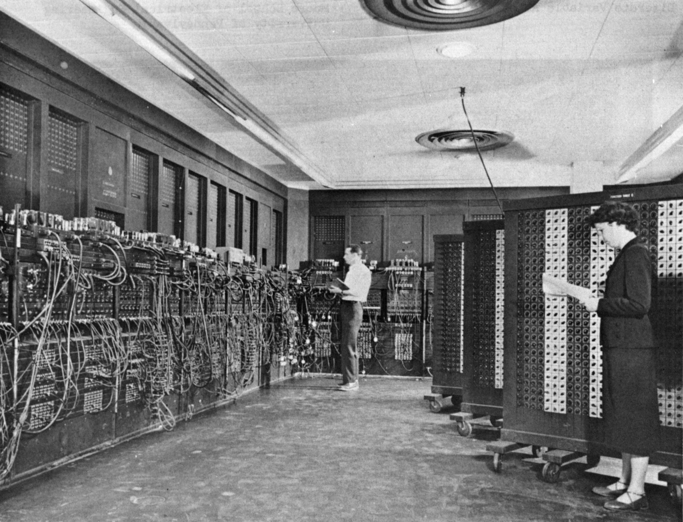 Two women stand at the panels of ENIAC, a wall-sized electronic computer of vacuum tubes and patch cables, Philadelphia 1946.
