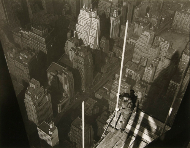 A worker high on the steel frame of the Empire State Building, hoisting the mast against the open sky, photographed by Lewis Hine.