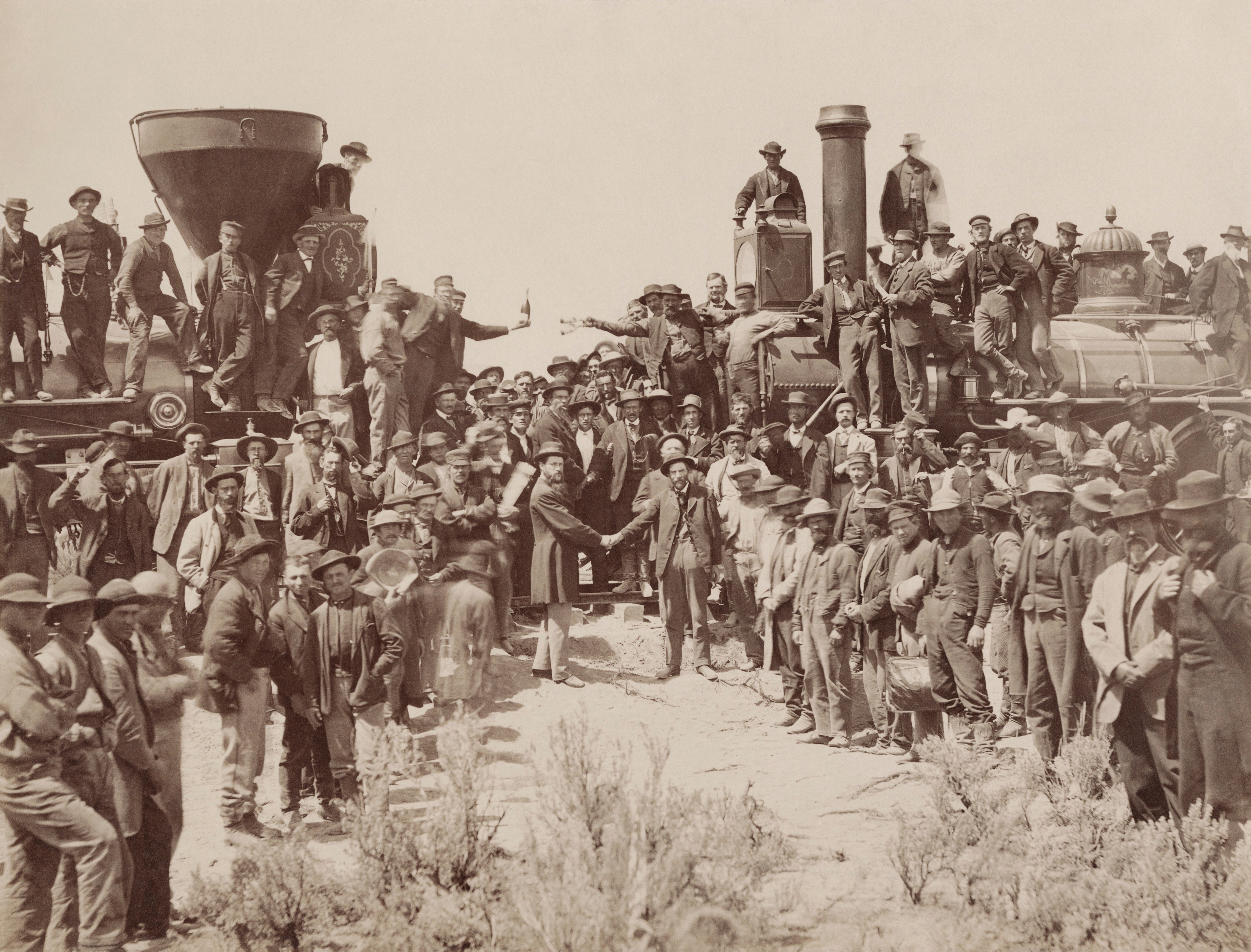 Two locomotives face each other nose-to-nose on a single track as crowds of workers and officials fill the foreground at Promontory Summit.