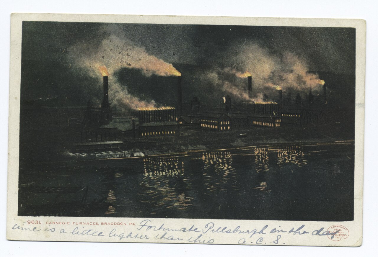 A panoramic view across the Monongahela River of the Carnegie Furnaces at Braddock, Pennsylvania, with a row of blast furnaces and rail yards along the riverbank, c. 1905.
