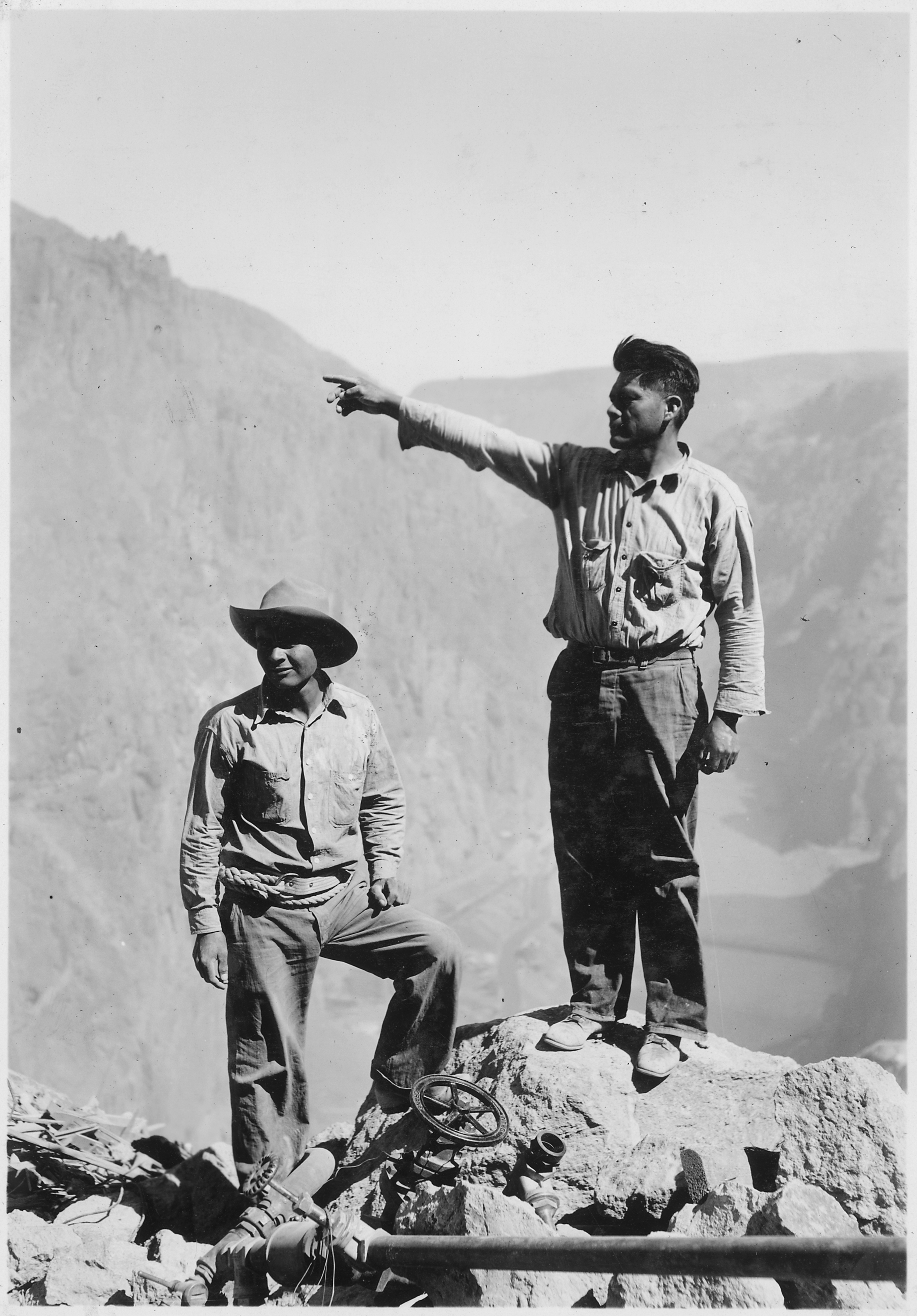 Indigenous high-scaler workers in coveralls and hard hats suspended by ropes against the bare canyon wall of the Hoover Dam construction site, 1932.
