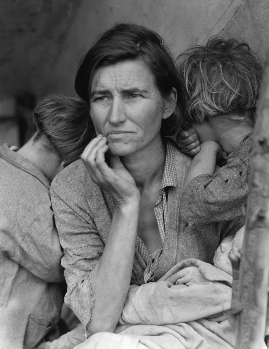 A mother with two children resting against her shoulders, gazing out from a migrant labor camp during the Great Depression.