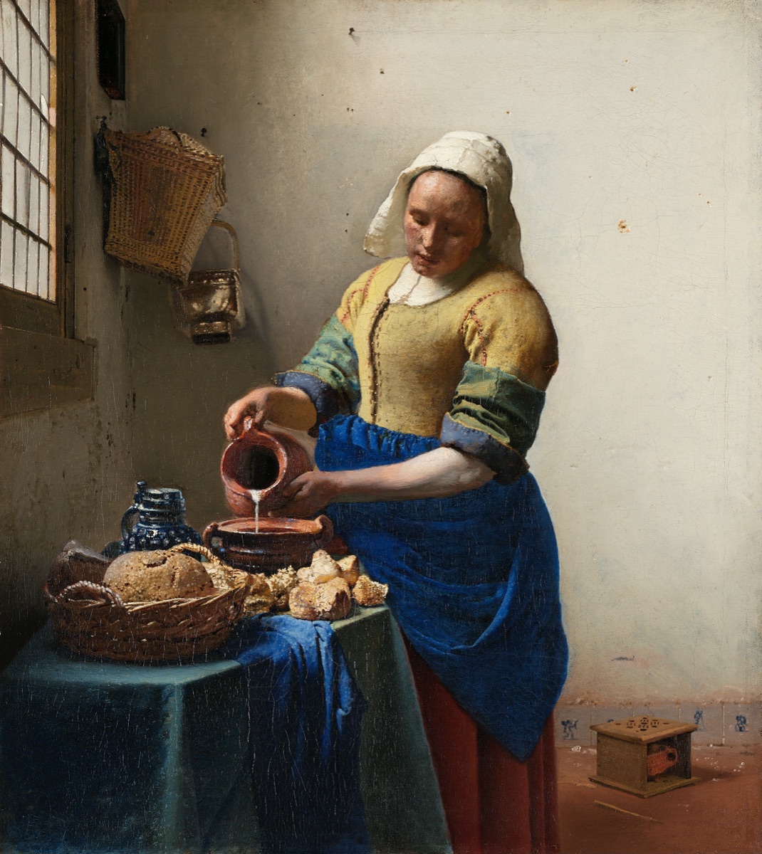 A Dutch maidservant pouring milk from a pitcher into an earthenware bowl at a sunlit table, painted by Vermeer around 1658.