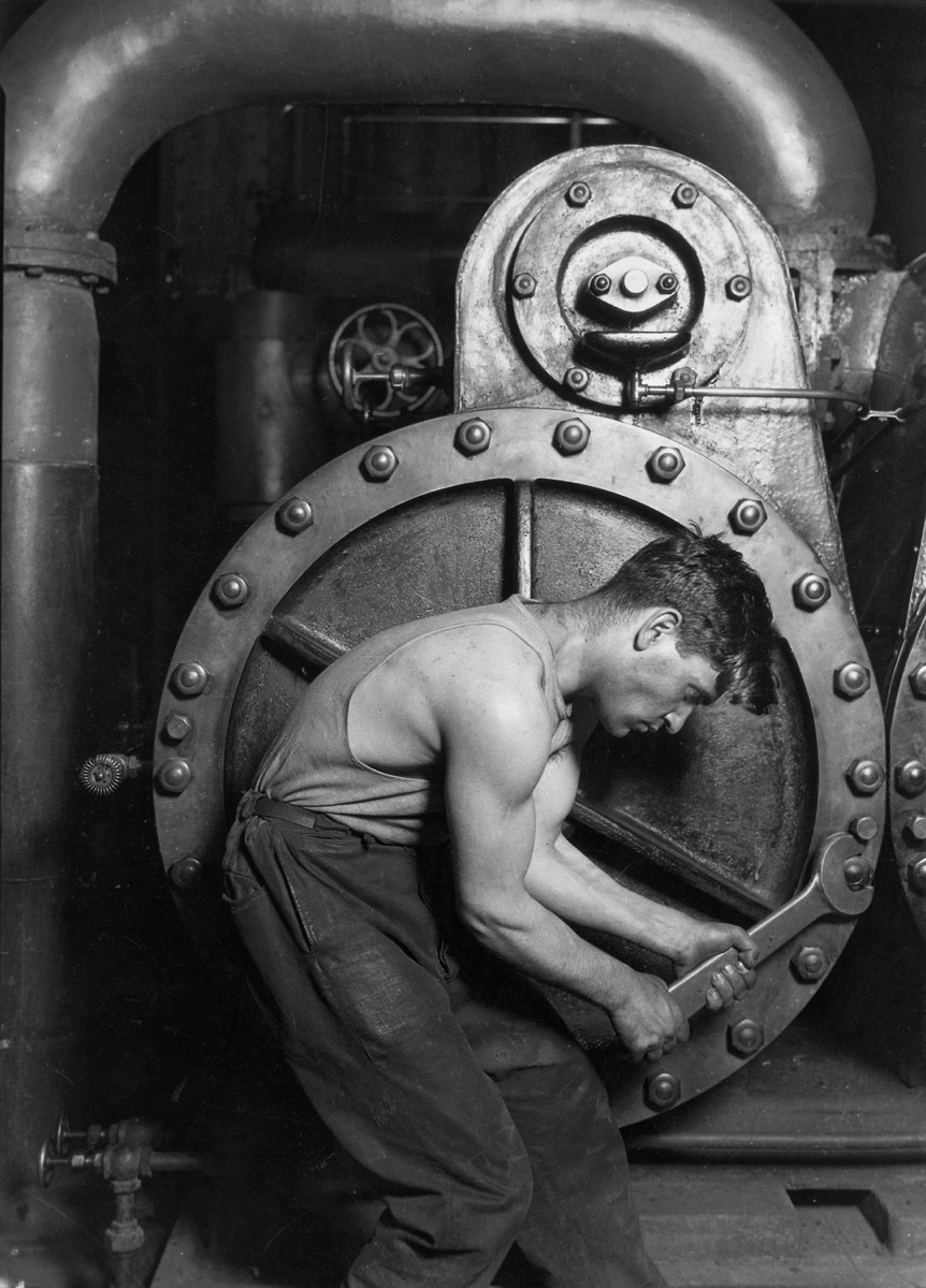 A muscular mechanic curved around a giant industrial steam pump, wrench in hand.