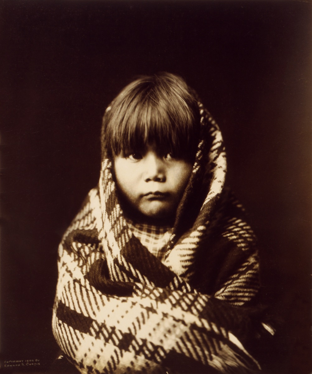 A photogravure portrait of a young Navajo child in traditional dress.