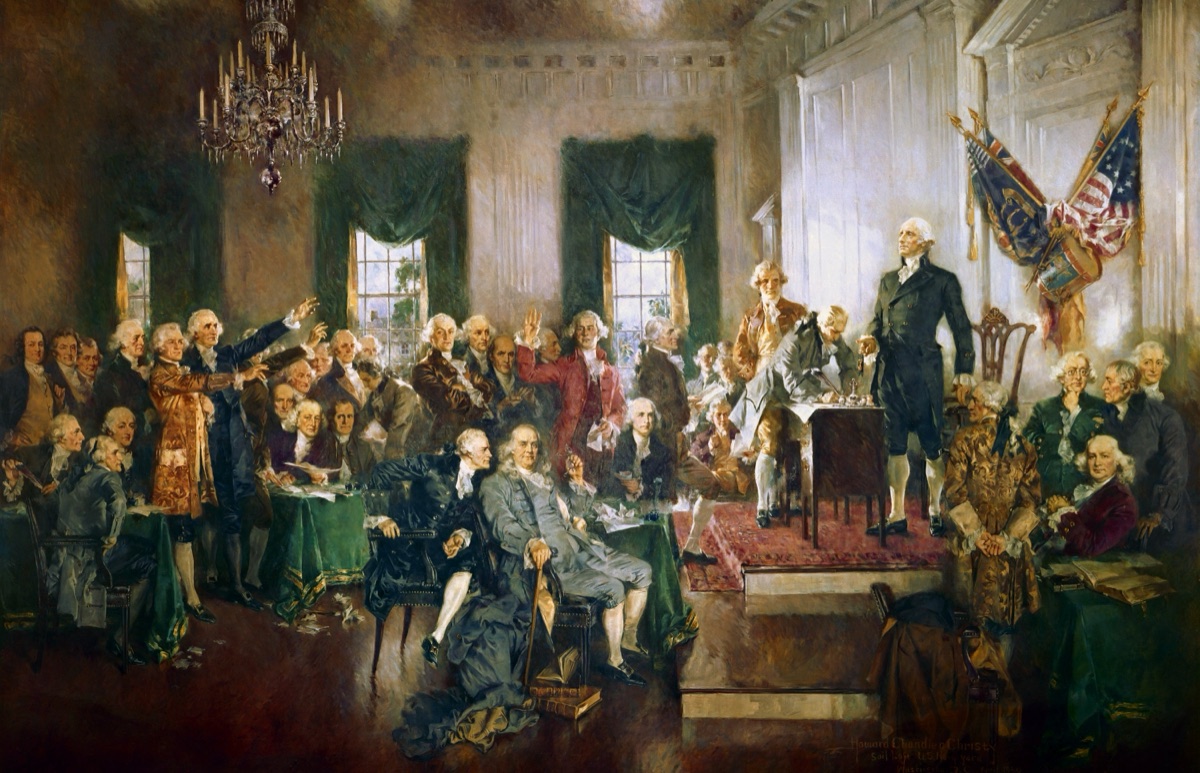 Delegates gathered at the front of a hall as George Washington presides over the signing of the U.S. Constitution.