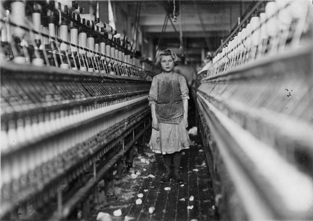 A young child standing beside a row of spinning frames in a Georgia cotton mill in 1909.